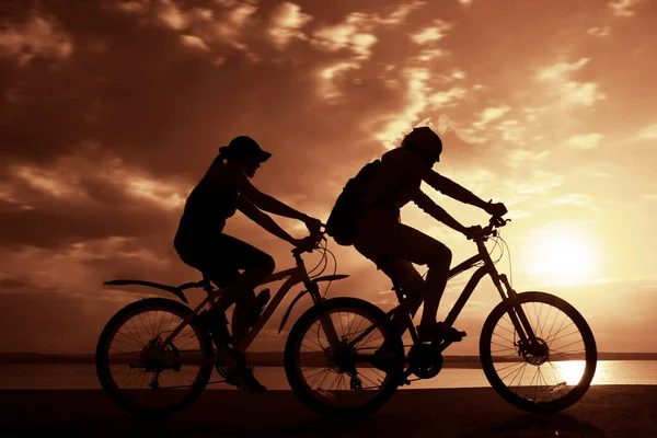 Sporty friends ride on bicycles. sunset sky. Silhouette of cyclist  on coast background. couple of people.