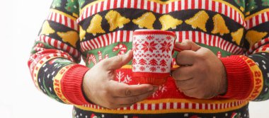 Sıcak çikolata içen bir adam. Noel ağacı deseni. Madalyalı içki kupası. Erkek, kırmızı fincanda sıcak kahve tutan örgü süveter ve Xmas süsü giyiyor. Eşcinseller kış tatillerini kutlar. Yüzü yok