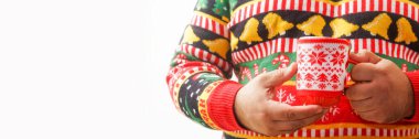 Sıcak çikolata içen bir adam. Noel ağacı deseni. Madalyalı içki kupası. Erkek, kırmızı fincanda sıcak kahve tutan örgü süveter ve Xmas süsü giyiyor. Eşcinseller kış tatillerini kutlar. Yüzü yok
