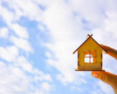 Erkek el ele tutuşuyor. Mavi güneşli arka planda ahşap ev modeli. Yazı için boş kopyalama alanı