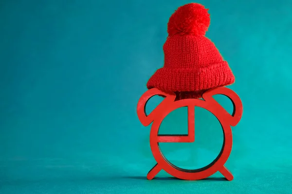 red alarm clock in a red knitted hat on  paper background. Concept of happy New Year year and merry Christmas