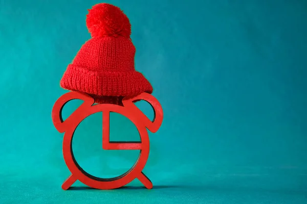 red alarm clock in a red knitted hat on  paper background. Concept of happy New Year year and merry Christmas