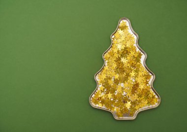 Yeşil kağıt arka planda izole edilmiş birçok altın konfeti noel ağacı biçimindedir..