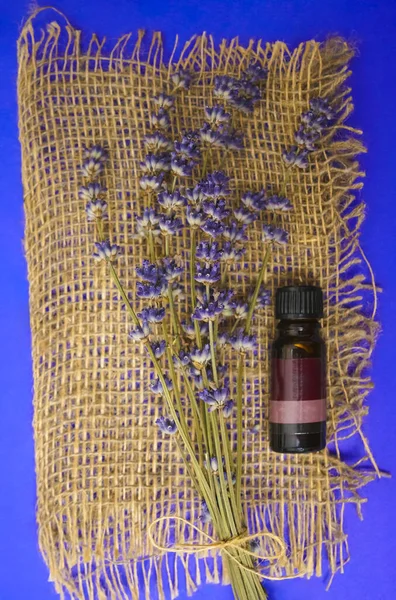Bunch of lavender flowers and bottle of essential oil on sackcloth background in a spa composition.