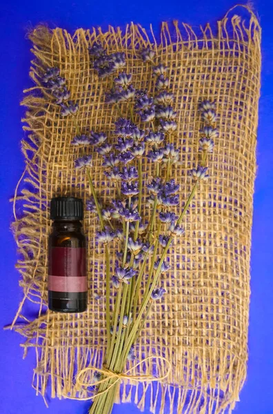 Bunch of lavender flowers and bottle of essential oil on sackcloth background in a spa composition.