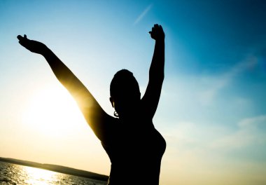 Şafak vakti, deniz kıyısında el kaldıran ve ayakta duran siluet kadın.