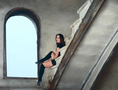 Güzel Latin dansçı kadın merdivenlerde dinleniyor. Siyah elbiseli genç kız beton merdivenlerde oturuyor.