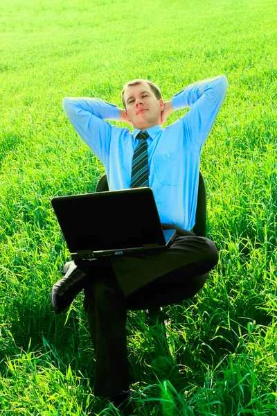 Businessman in the field, with a laptop. Happy, successful. Business man sitting on a chair in green grass field. closed eyes.