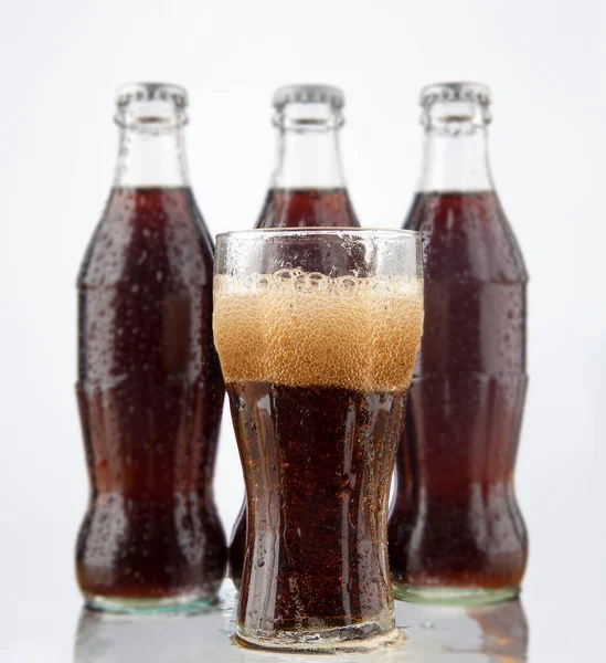 three Cola  bottles  and transparent glass with bubbles  isolated on white background.
