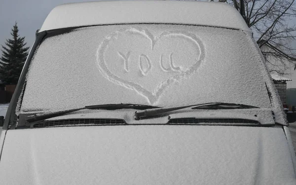 新鮮なクリスマスの雪で覆われた車のフロントガラスに描かれた心 窓のワイパーや雪に覆われた車やバス 冬のシーズン 正面の眺め ハッピーバレンタインデー 2月14日 — ストック写真