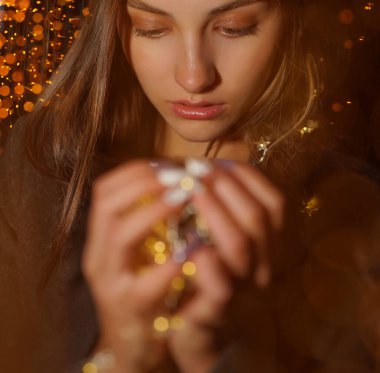 Kız elinde çelenk tutuyor. Gece sahnesi. Sarı Noel ışığı tutan rüya gibi kadın elleri, bokeh arka plan. Bulanık ve bokeh arkaplanlı LED noel ışıkları 