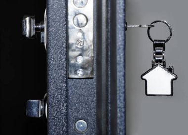 Kapının kilidinde metal süs eşyası olan anahtar. Kapı yarı açık. Arka plan bulanık. Kiralık emlak.