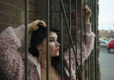 Latin asıllı, güzel bir kadın, demir parmaklıklardan dışarı bakıyor. Güzellik, moda. Kilitli. kapalı alan