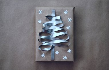 Noel ağacı şeklinde gümüş kurdeleyle süslenmiş bir hediye kutusu. el işi kâğıdı. beyaz kar taneleri