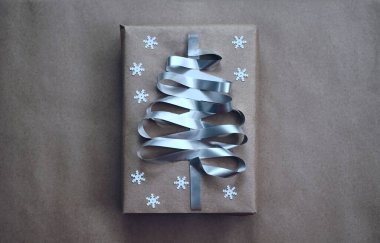 Noel ağacı şeklinde gümüş kurdeleyle süslenmiş bir hediye kutusu. el işi kâğıdı. beyaz kar taneleri