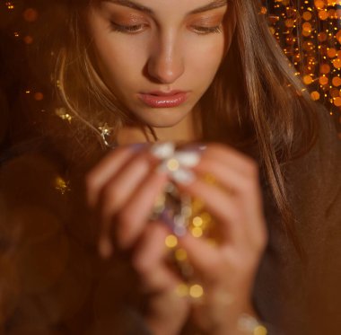 Kız elinde çelenk tutuyor. Gece sahnesi. Sarı Noel ışığı tutan rüya gibi kadın elleri, bokeh arka plan. Bulanık ve bokeh arkaplanlı LED noel ışıkları 