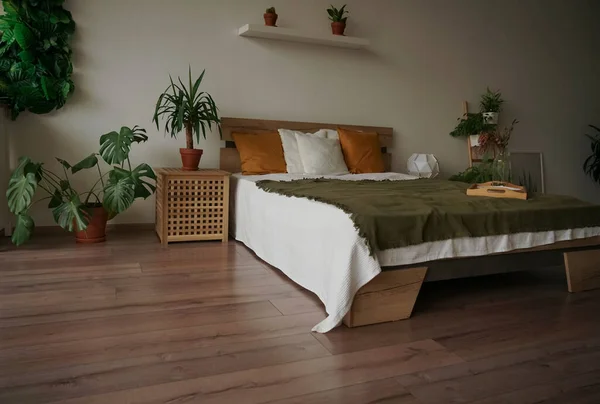 bedroom in soft light colors. big comfortable double bed in elegant classic bedroom. many green plants. natural wooden materials.