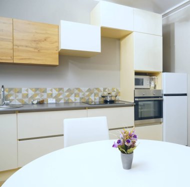 Mutfağa yakın vazolu yemek masası buzdolabı, zemin tasarım, elektrik, soba duvarda asılı vazo, yemek masasında çiçek saksısı ve seramik tabak, beyaz renkli sandalye.