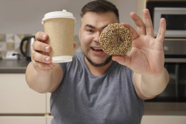 Mutfak geçmişindeki mutlu sakallı adam. Orta yaşlı erkek. Tatlı çörek ve kahve fincanı. Çikolatalı çörek. Diyet yaparken cezbedici. Tatlı hayat..  