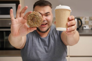 Mutfak geçmişindeki mutlu sakallı adam. Orta yaşlı erkek. Tatlı çörek ve kahve fincanı. Çikolatalı çörek. Diyet yaparken cezbedici. Tatlı hayat..  