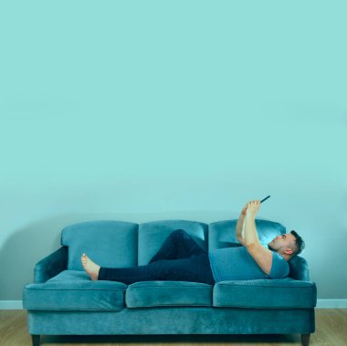 Orta yaşlı bir adam hücre ekranına bakıyor, akıllı telefon ve kanepede dinleniyor..