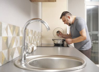 Bir adam karantinada kaynamış suyun kapağını kaldırır. Arka planda mutfak içi