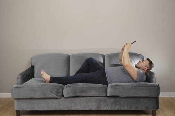middle aged man looking at screen of cell, smartphone and relax on couch.