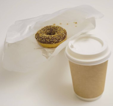 Paket paketinde bir çikolatalı çörek ve beyaz masada bir fincan kahve. Lezzetli çöller toz fındıkla kaplı, bir sokak fast food 'undan alınmış..