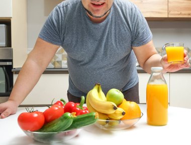 Orta yaşlı bir adam masada taze sıkılmış meyve suyu yapıyor. meyve ve sebze. Bir şişe ve bir bardak portakal suyu. Erkek, şişeden cama portakal suyu döküyor..
