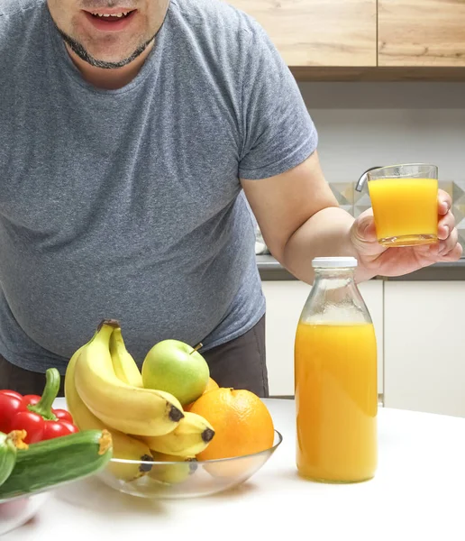 中年男人在桌子上做新鲜榨果汁 水果和蔬菜 瓶子和一杯橙汁 男人把橙汁从瓶子倒到杯子里 — 图库照片