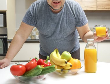 Orta yaşlı bir adam masada taze sıkılmış meyve suyu yapıyor. meyve ve sebze. Şişe ve bir bardak portakal suyu..