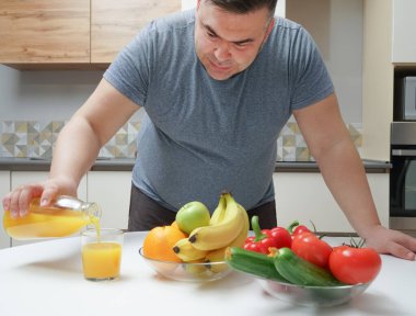 Orta yaşlı bir adam masada taze sıkılmış meyve suyu yapıyor. meyve ve sebze. Bir şişe ve bir bardak portakal suyu. Erkek, şişeden cama portakal suyu döküyor..