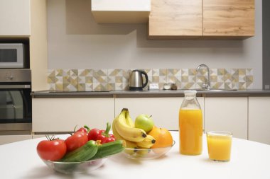 Modern stil mutfak içinde sebzeler ve beyaz ahşap masada meyveler. Parlak beyaz mutfak ve ev eşyaları. Sağlıklı yaşam tarzı kavramı. Yiyecek ve içecek.