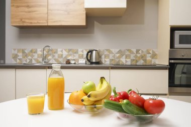 Modern stil mutfak içinde sebzeler ve beyaz ahşap masada meyveler. Parlak beyaz mutfak ve ev eşyaları. Sağlıklı yaşam tarzı kavramı. Yiyecek ve içecek.