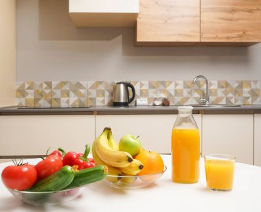 Modern stil mutfak içinde sebzeler ve beyaz ahşap masada meyveler. Parlak beyaz mutfak ve ev eşyaları. Sağlıklı yaşam tarzı kavramı. Yiyecek ve içecek.