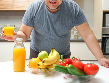 Orta yaşlı bir adam masada taze sıkılmış meyve suyu yapıyor. meyve ve sebze. Şişe ve bir bardak portakal suyu..