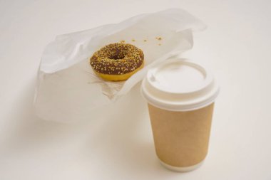 Paket paketinde bir çikolatalı çörek ve beyaz masada bir fincan kahve. Lezzetli çöller toz fındıkla kaplı, bir sokak fast food 'undan alınmış..