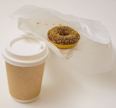 Paket paketinde bir çikolatalı çörek ve beyaz masada bir fincan kahve. Lezzetli çöller toz fındıkla kaplı, bir sokak fast food 'undan alınmış..