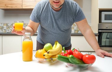 Orta yaşlı bir adam masada taze sıkılmış meyve suyu yapıyor. meyve ve sebze. Şişe ve bir bardak portakal suyu..