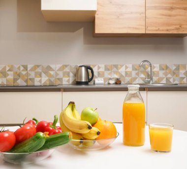 Modern stil mutfak içinde sebzeler ve beyaz ahşap masada meyveler. Parlak beyaz mutfak ve ev eşyaları. Sağlıklı yaşam tarzı kavramı. Yiyecek ve içecek.