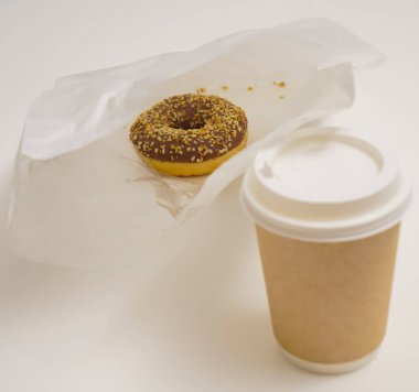 Paket paketinde bir çikolatalı çörek ve beyaz masada bir fincan kahve. Lezzetli çöller toz fındıkla kaplı, bir sokak fast food 'undan alınmış..