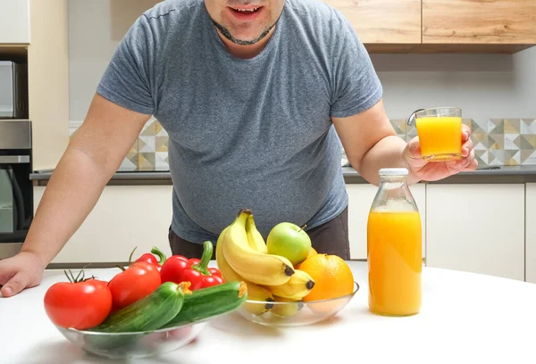 middle aged man making freshly squeezed juice on a table. fruit and vegetable. bottle and glass of orange juice.