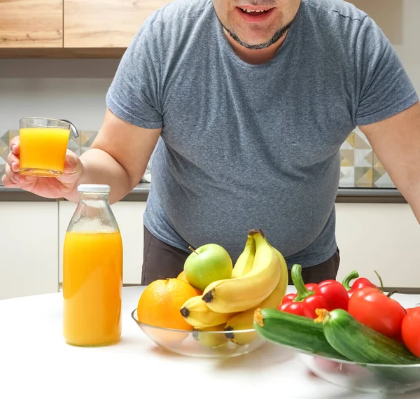 中年男人在桌子上做新鲜榨果汁 水果和蔬菜 瓶子和一杯橙汁 — 图库照片