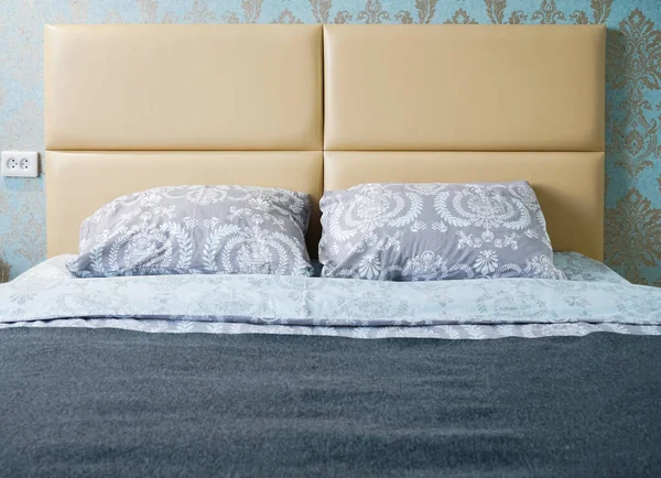 Interior with blue bed linen on the double bed. Bedroom with bed, white bedding.  Gray pillows, duvet and duvet case on bed with beige headboard. Front view.