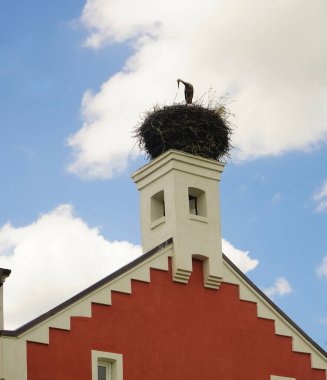 Küçük bir köyün sütunlarından birinde yuvasında bir leylek. Mavi gökyüzü. Köyün doğası. Çatıda leylek var. MAMONOVO. Kalininingrad bölgesi                 