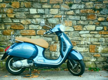 Güzel klasik tasarım gri renkli Vespa scooter, taştan duvar zeminine park etmiş bej koltuklu minder. SALZBURG, AUSTRIA