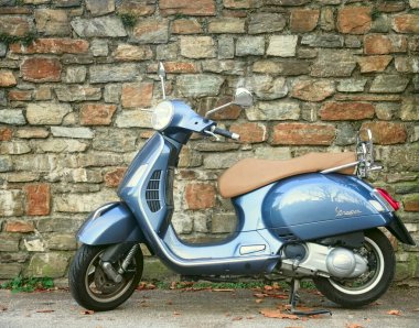 SALZBURG, AUSTRIA - 06 Aralık 2019: Taş duvar arka planında bej koltuk minderi olan güzel klasik tasarım gri Vespa scooter