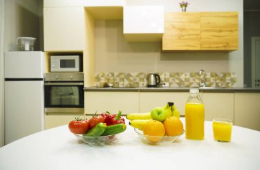 Modern stil mutfak içinde sebzeler ve beyaz ahşap masada meyveler. Parlak beyaz mutfak ve ev eşyaları. Sağlıklı yaşam tarzı kavramı. Yiyecek ve içecek..