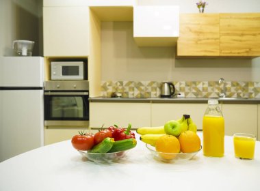 Modern stil mutfak içinde sebzeler ve beyaz ahşap masada meyveler. Parlak beyaz mutfak ve ev eşyaları. Sağlıklı yaşam tarzı kavramı. Yiyecek ve içecek..