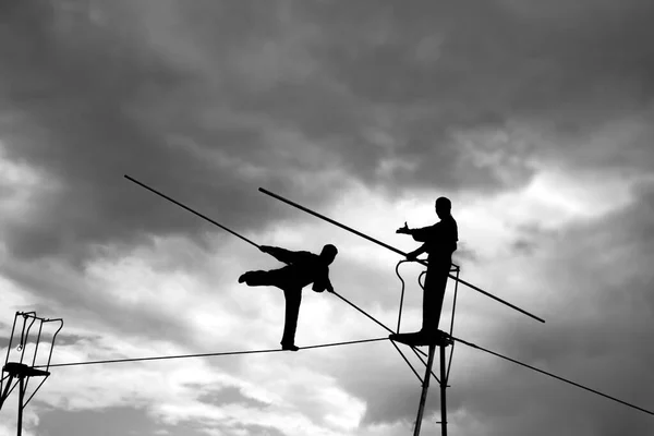 Wandering tightrope walkers playing on sky background. Silhouette of Equilibrist businessmen with pole on the rope. idea concept of help and insurance, belay in business. Show in air